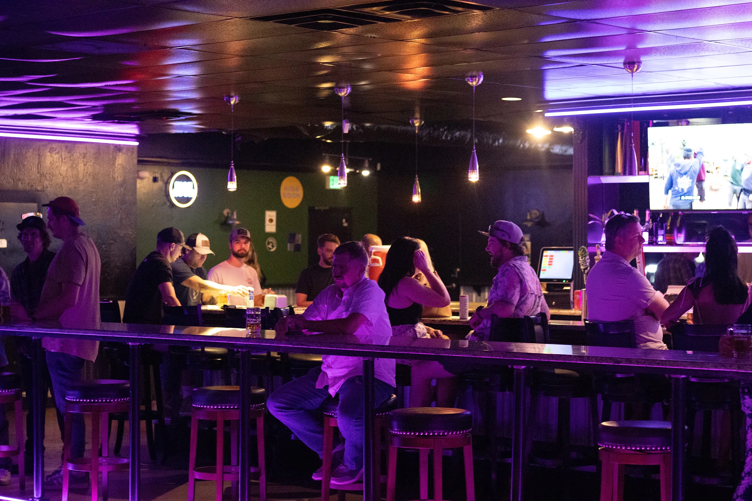 The bar at The Midnight Toad on a busy night, lit purple, with people along the rail and staff pouring behind it.
